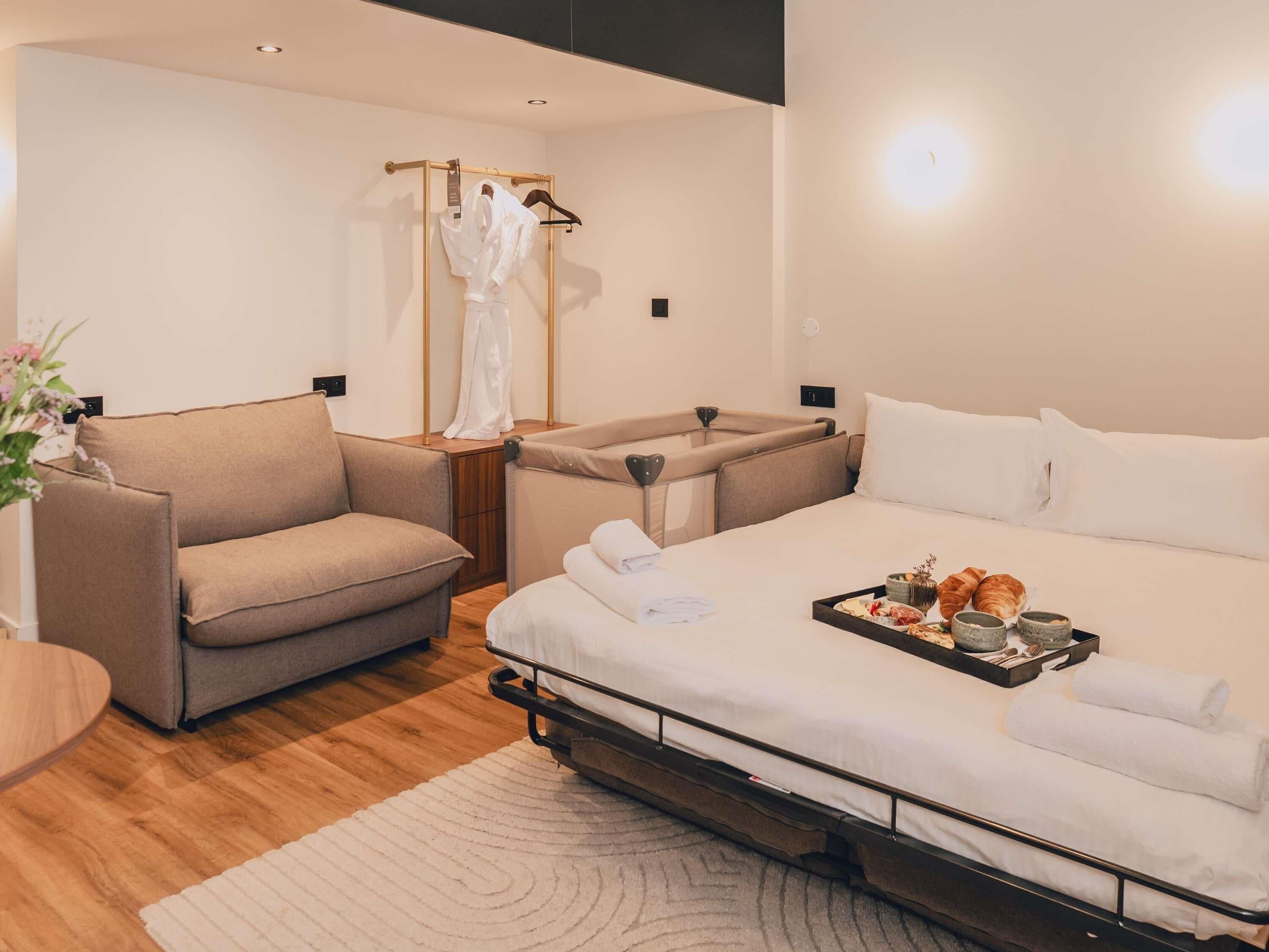 A modern hotel room with a sofa, a bed with a tray of breakfast, and a robe rack.