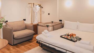 A modern hotel room with a sofa, a bed with a tray of breakfast, and a robe rack.