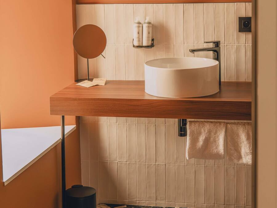 Un baño moderno con tocador de madera, un espejo redondo, un lavabo blanco y una toalla colgada en un perchero.