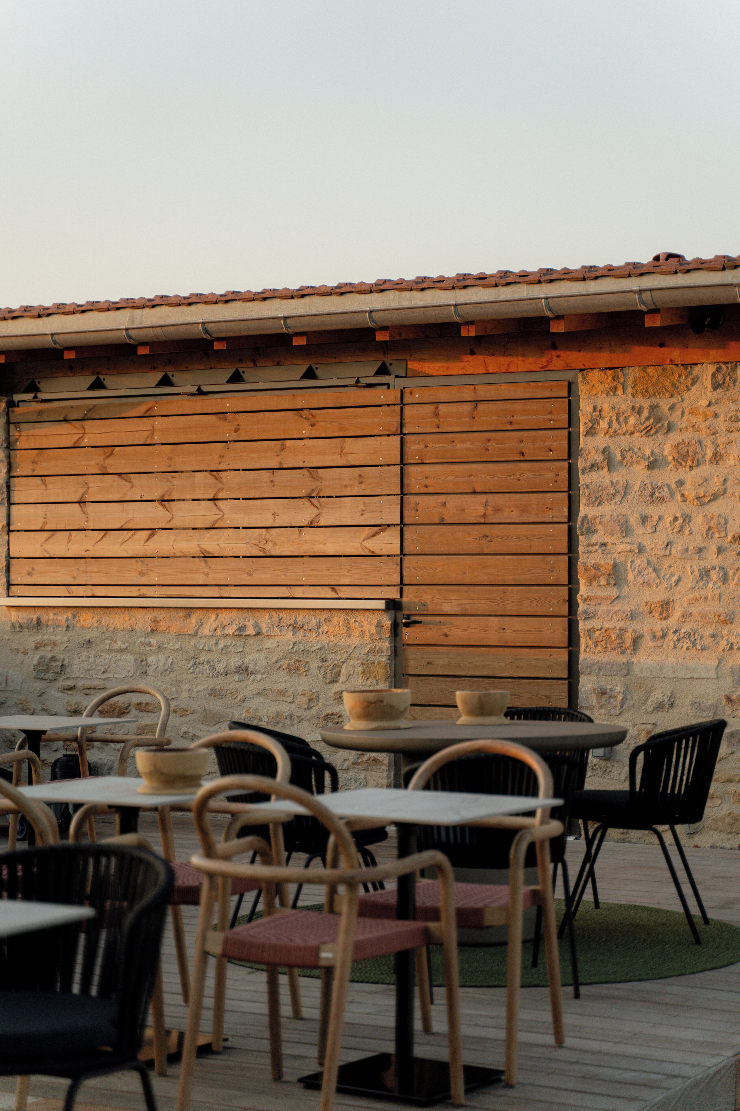 Un espacio al aire libre con mesas y sillas, un muro de piedra y un muro de listones de madera.