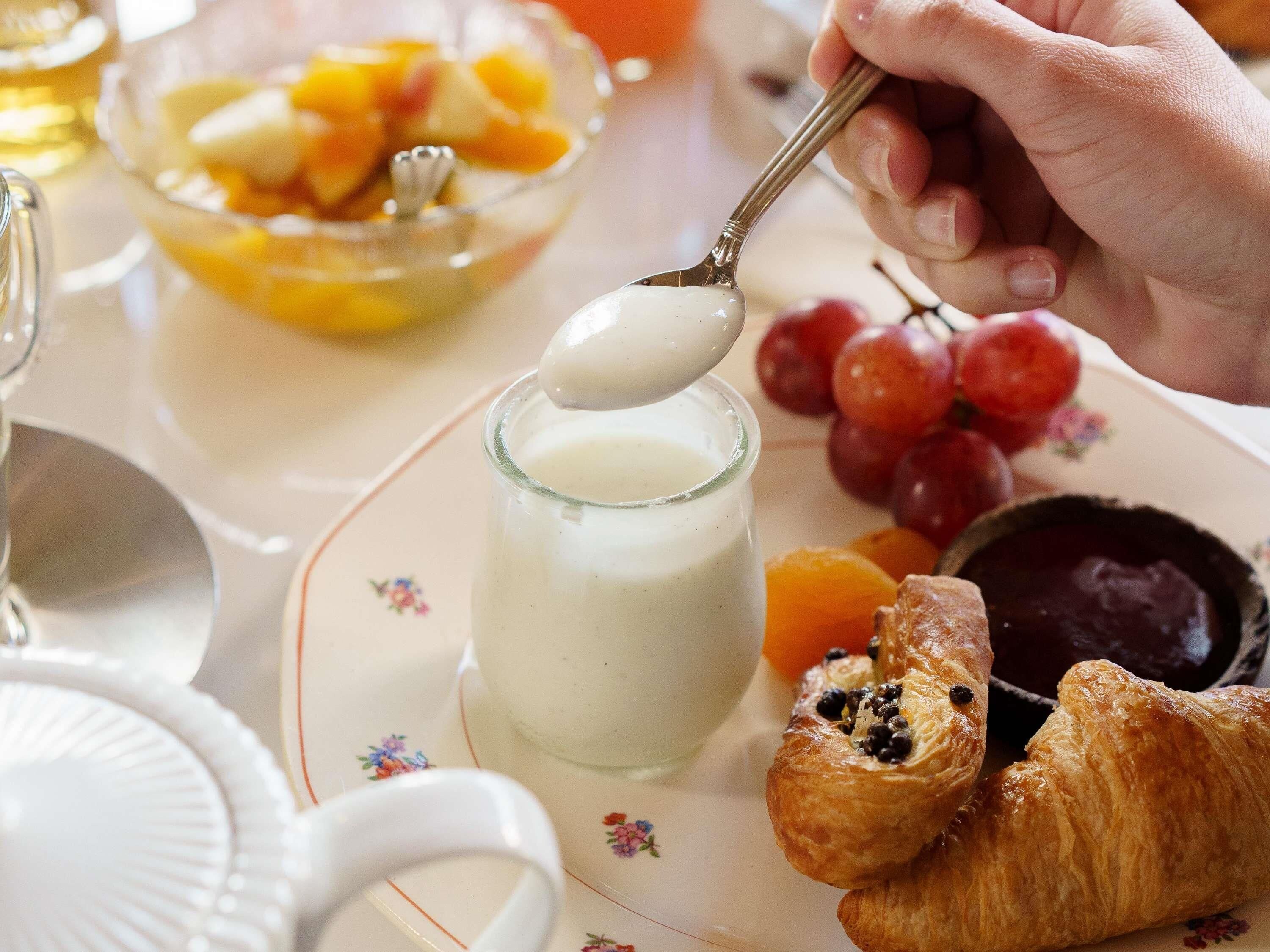 Ein Frühstückstisch mit Glas Milch, Obstschale und Gebäck auf einer blumigen Tischdecke.