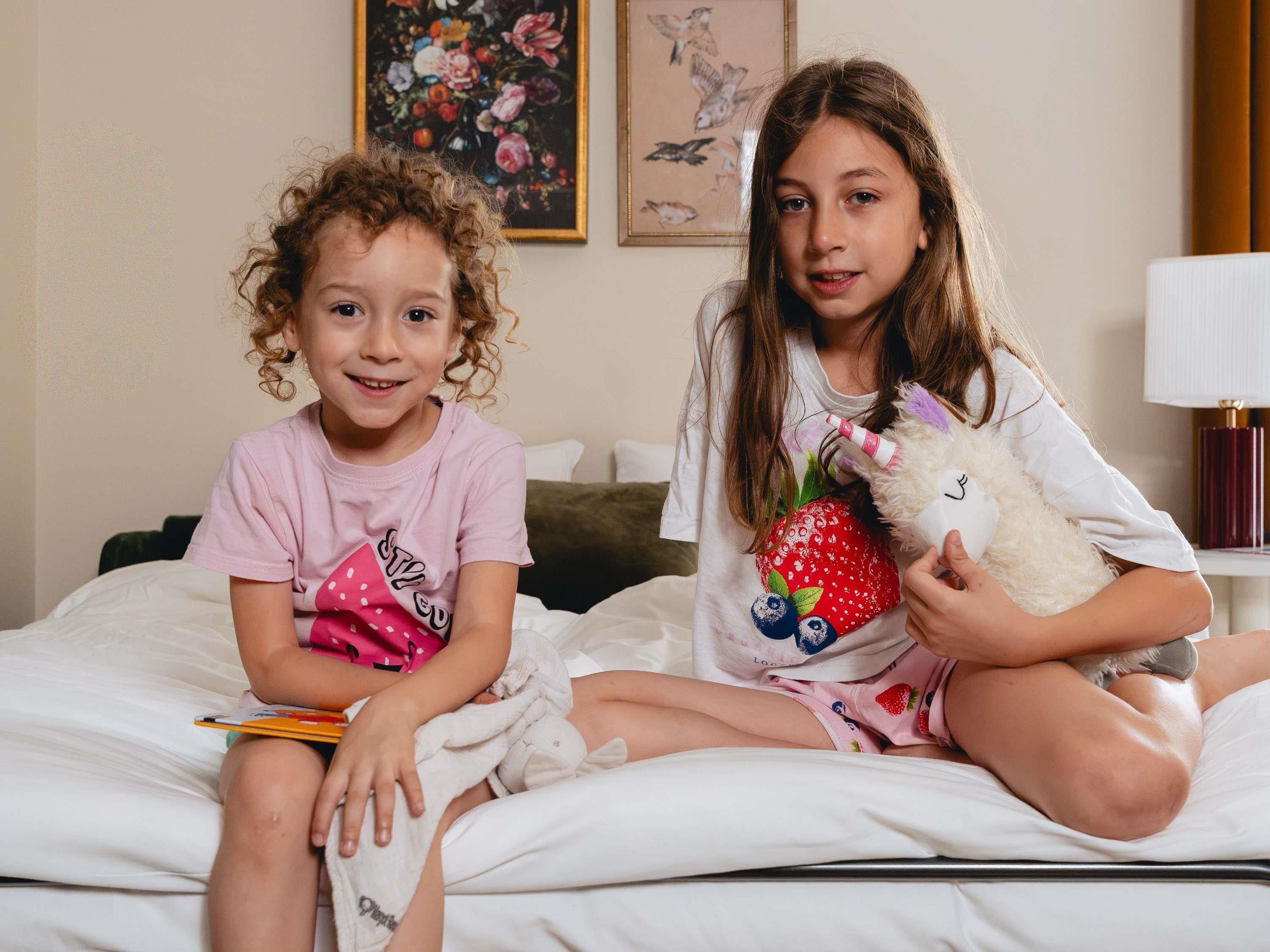 Dos niños sentados en una cama en una habitación con un cuadro en la pared.