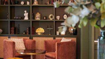 Een kamer met een zithoek, een klein rond tafeltje en een boekenplank vol decoratieve objecten.