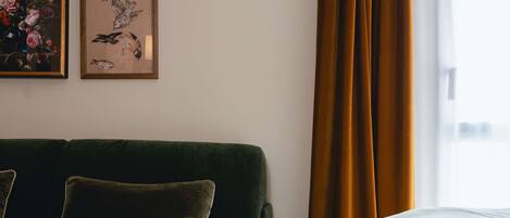 A room with a green sofa, a small table with a magazine, and a bed with a white comforter.