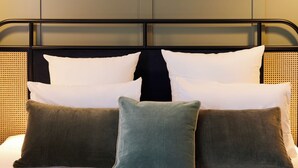 A bed with white and green pillows, a headboard with a woven pattern, and framed artwork on the wall above. - Square Lodge Hotel La Roche Sur Yon - Handwritten Collection (La Roche-sur-Yon)
