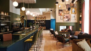 Eine Bar mit Tresen, Hockern und Regalen mit Flaschen und Gläsern. Es gibt eine Sitzecke mit einer Couch und Sesseln, sowie eine Wand mit gerahmten Bildern.