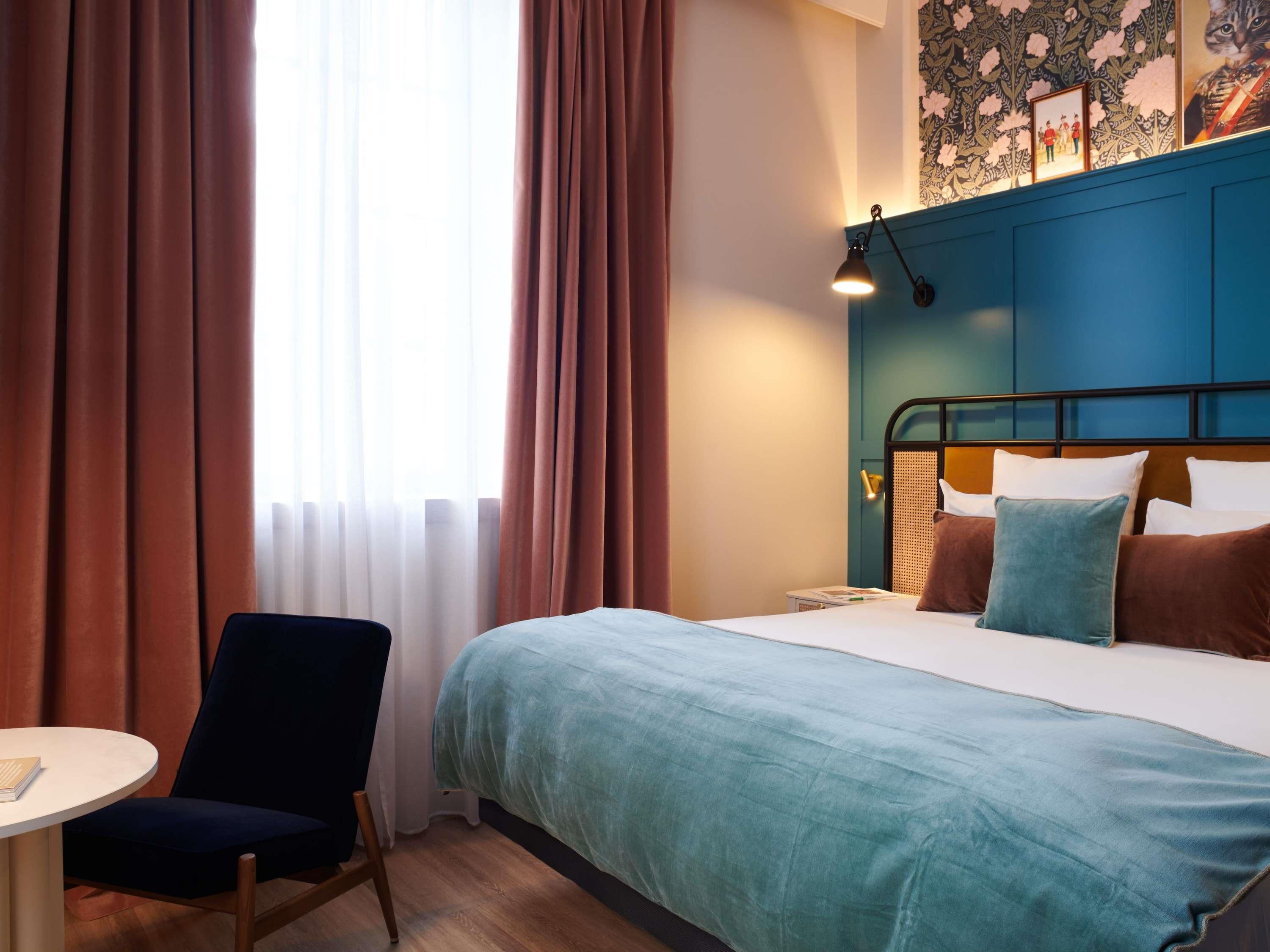 Una habitación de hotel con una cama, una silla, una mesa y un ventanal con cortinas.