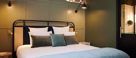 Una cama bien arreglada con una manta azul, una pared con papel tapiz floral y dos lámparas de pared para leer.