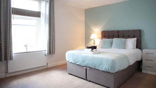 Een slaapkamer met een bed, een bedlampje en een raam met gordijnen.