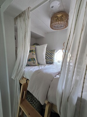 Un dormitorio con cama, almohadas, un banco de madera y una lámpara colgante.