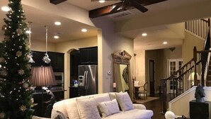 A living room with a beige sofa, a Christmas tree, a kitchen area, and a staircase.
