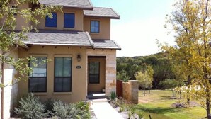 A two-story house with a stone facade, a front entrance, and a landscaped yard with shrubs and a tree.