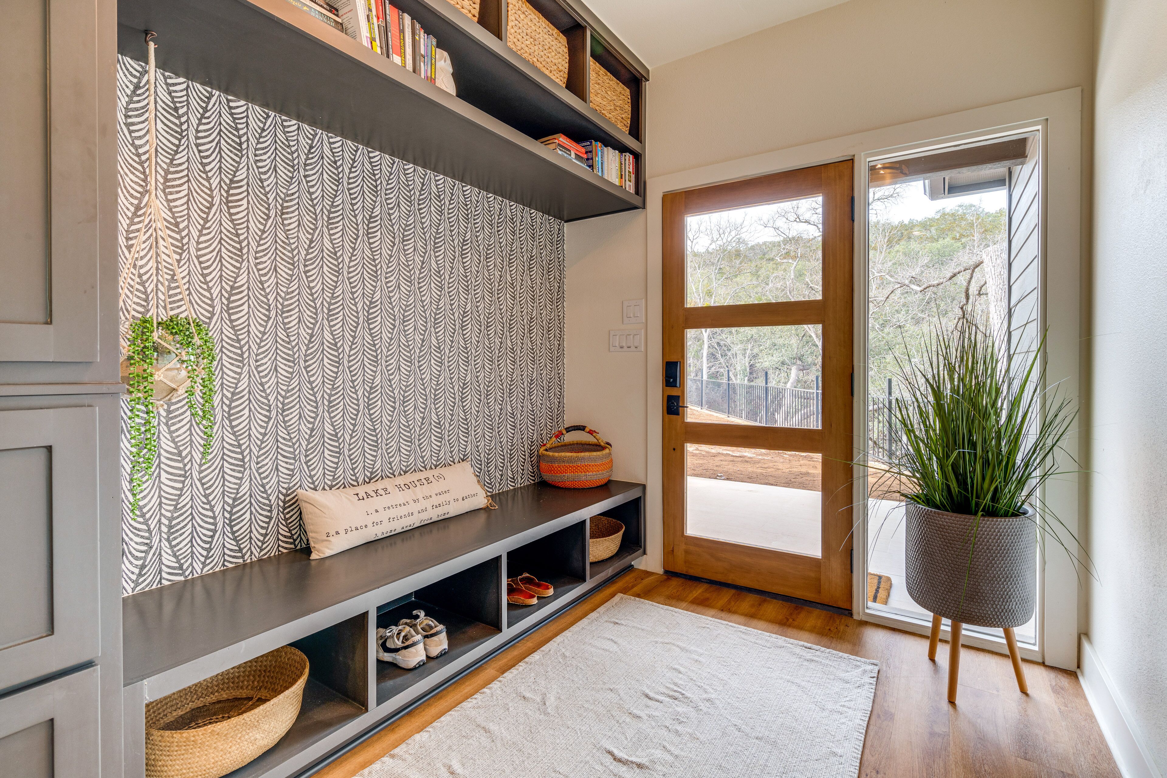 A modern entryway with a patterned wallpaper, a console table with baskets, a potted plant, and a wooden door.