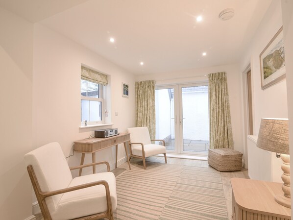 A room with a large window, a radio, a chair, a small table, and a lamp. - Backlands Farmhouse (Bridport)