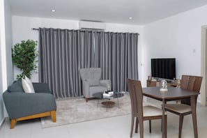 A modern living room with a grey sofa, a round coffee table, and a dining table with chairs. - Modern and stylish 2 bedroom apartment  (Accra)