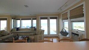 Ein geräumiges Wohnzimmer mit großem Fenster zum Meer, einer gemütlichen Sitzecke und einem Esstisch mit Stühlen.