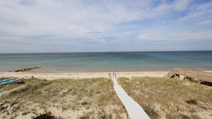Ein Strand mit einer Holzpromenade, die zum Wasser führt, feinem Sand und einem klaren Himmel.