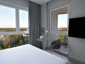 A modern hotel room with a large bed, a small round table with a chair, a desk lamp, and a flat-screen TV. - Novotel Lubumbashi (Lubumbashi)