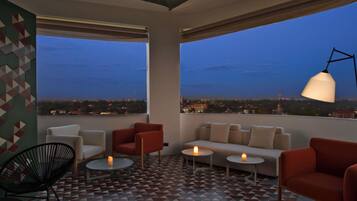 Terraço no telhado com sofá, cadeiras, mesas e um abajur.
