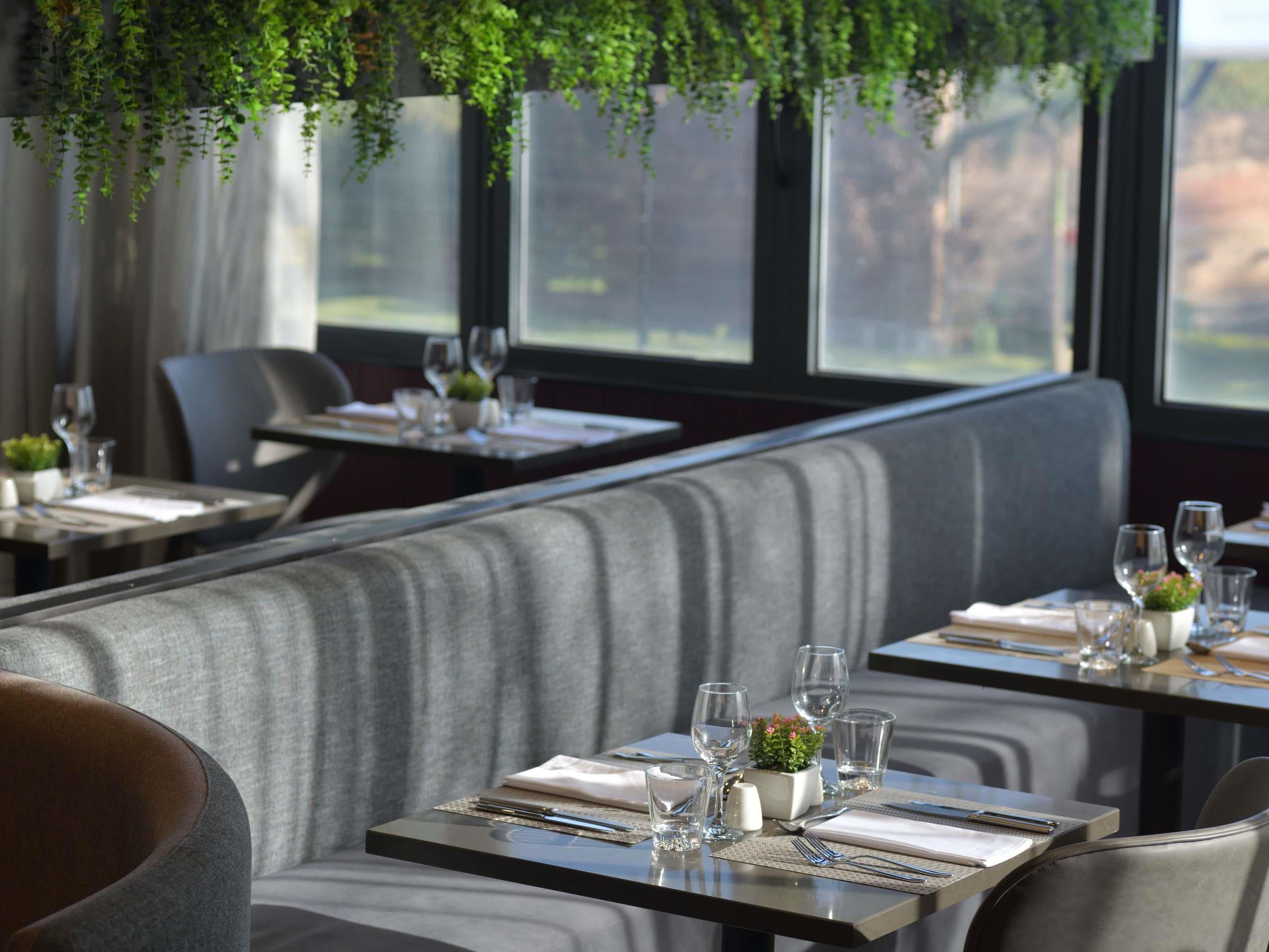 L’intérieur d’un restaurant avec des banquettes, des tables dressées avec des couverts, des verres et une petite plante posée sur chaque table.