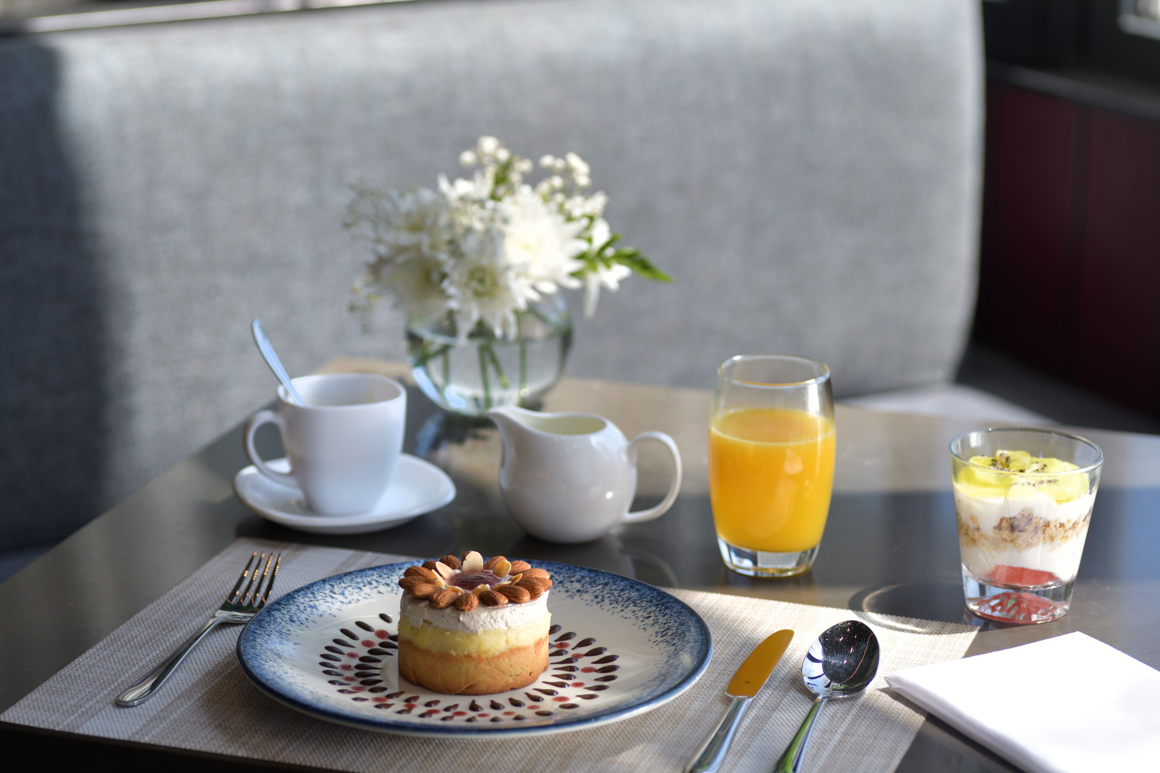 A table with a dessert, a cup of coffee, a pitcher, a glass of orange juice, and a glass of yogurt parfait.