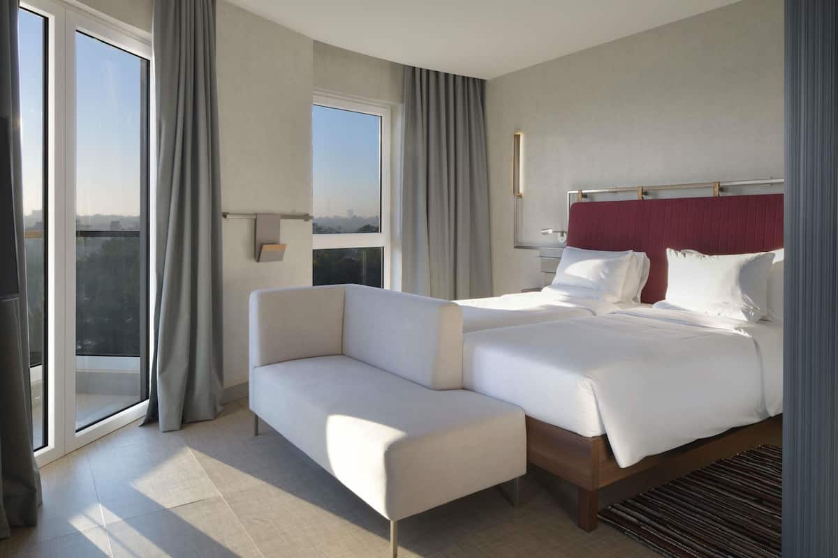 Ein Hotelzimmer mit Bett, Sofa, Fenster mit Vorhängen, Nachttisch und Blick auf die Stadt.