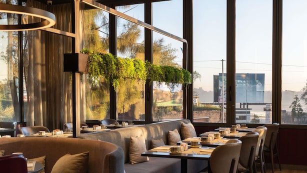 A modern restaurant with large windows, a sofa, and dining tables set for guests. - Novotel Lubumbashi (Lubumbashi)