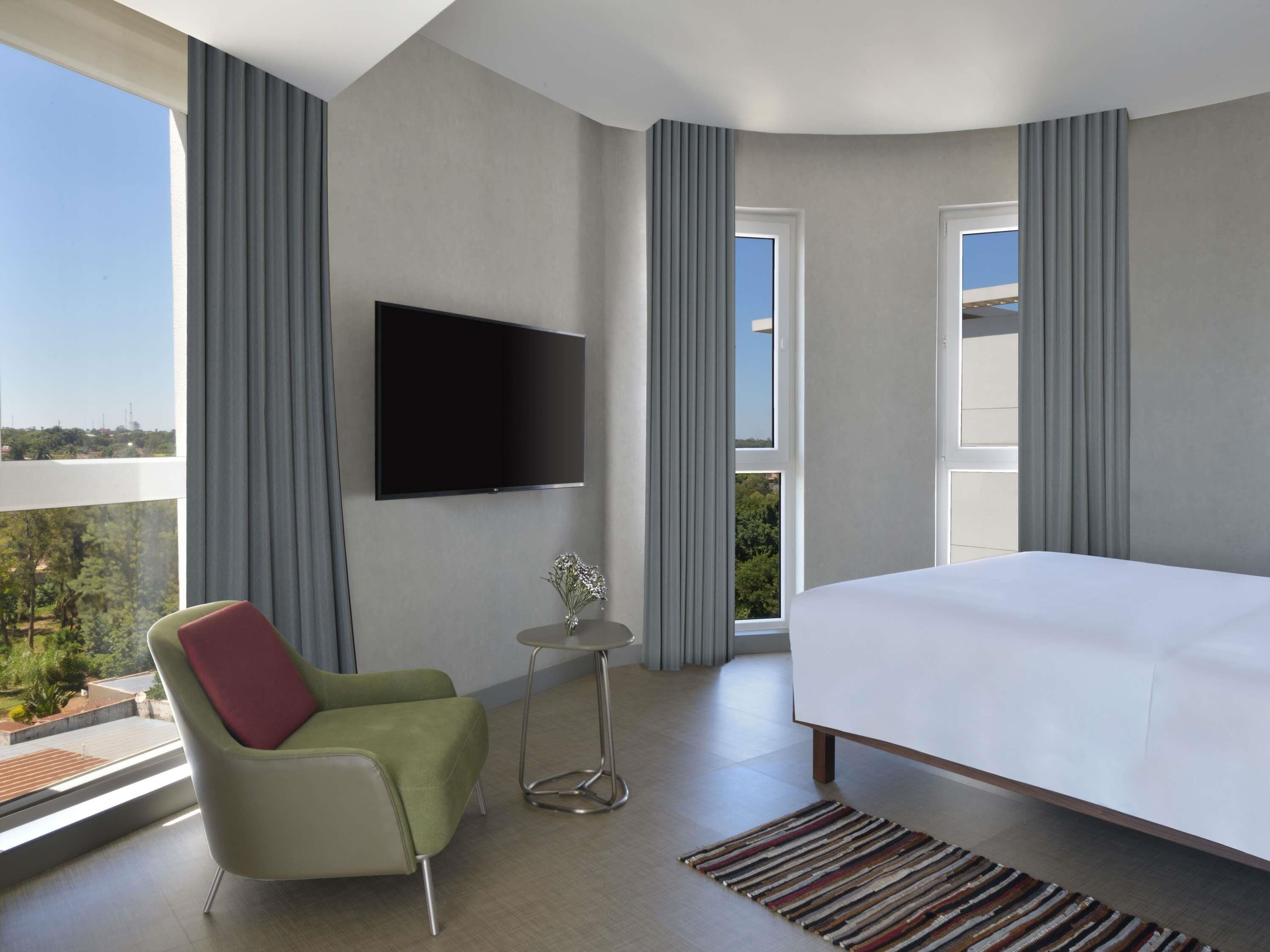 Une chambre d’hôtel moderne, équipée d’un lit, d’un téléviseur fixé au mur, d’une petite table avec un vase et d’une chaise.