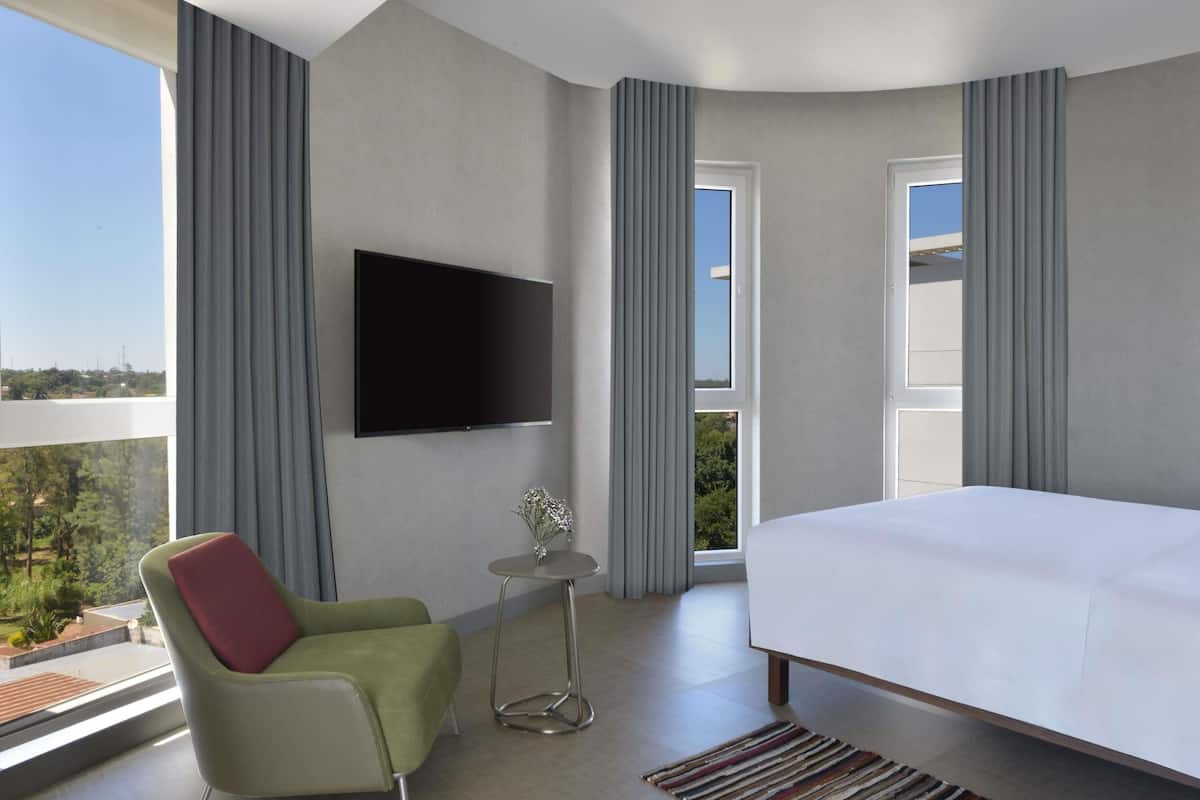 Une chambre dâhĂŽtel moderne, Ă©quipĂ©e dâun lit, dâun tĂ©lĂ©viseur fixĂ© au mur, dâune petite table avec un vase et dâune chaise.