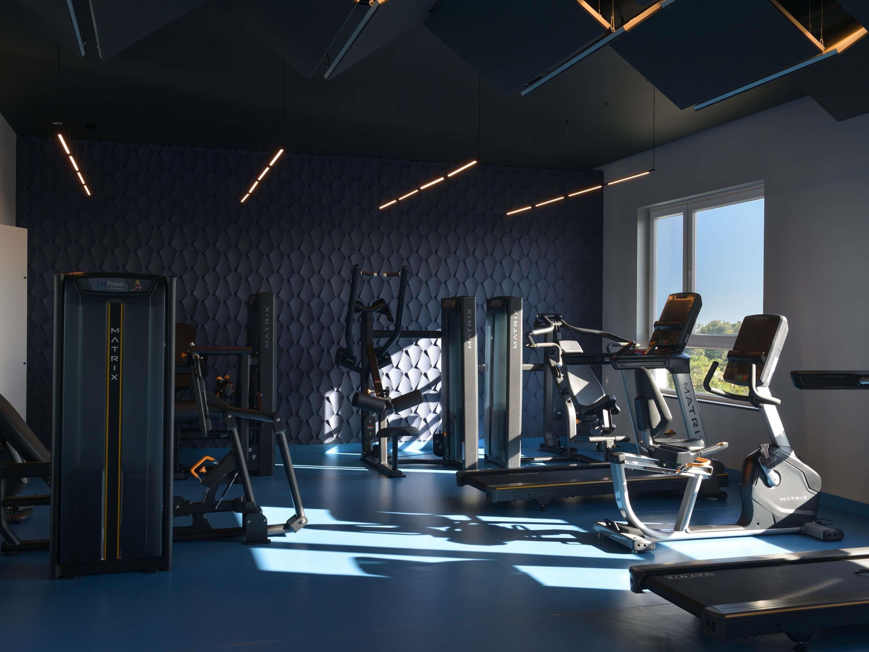 A modern gym with various exercise equipment, a patterned wall, and a large window providing natural light.