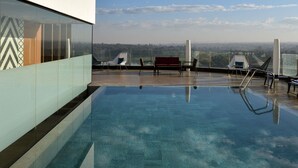 A rooftop pool with clear blue water, surrounded by lounge chairs and a view of a distant landscape. - Novotel Lubumbashi (Lubumbashi)