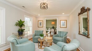 A spacious living room with light blue armchairs, a round coffee table, and a large mirror.