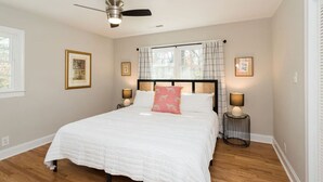 A bedroom with a large bed, two bedside lamps, a ceiling fan, and framed pictures on the walls.