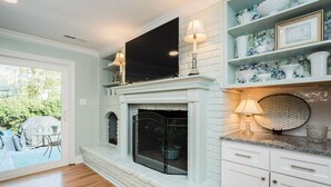 A modern living room with a fireplace, a flat-screen TV mounted above it, and a dining area with a table and chairs.