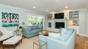 A living room with a fireplace, a television, and a large painting of flamingos.