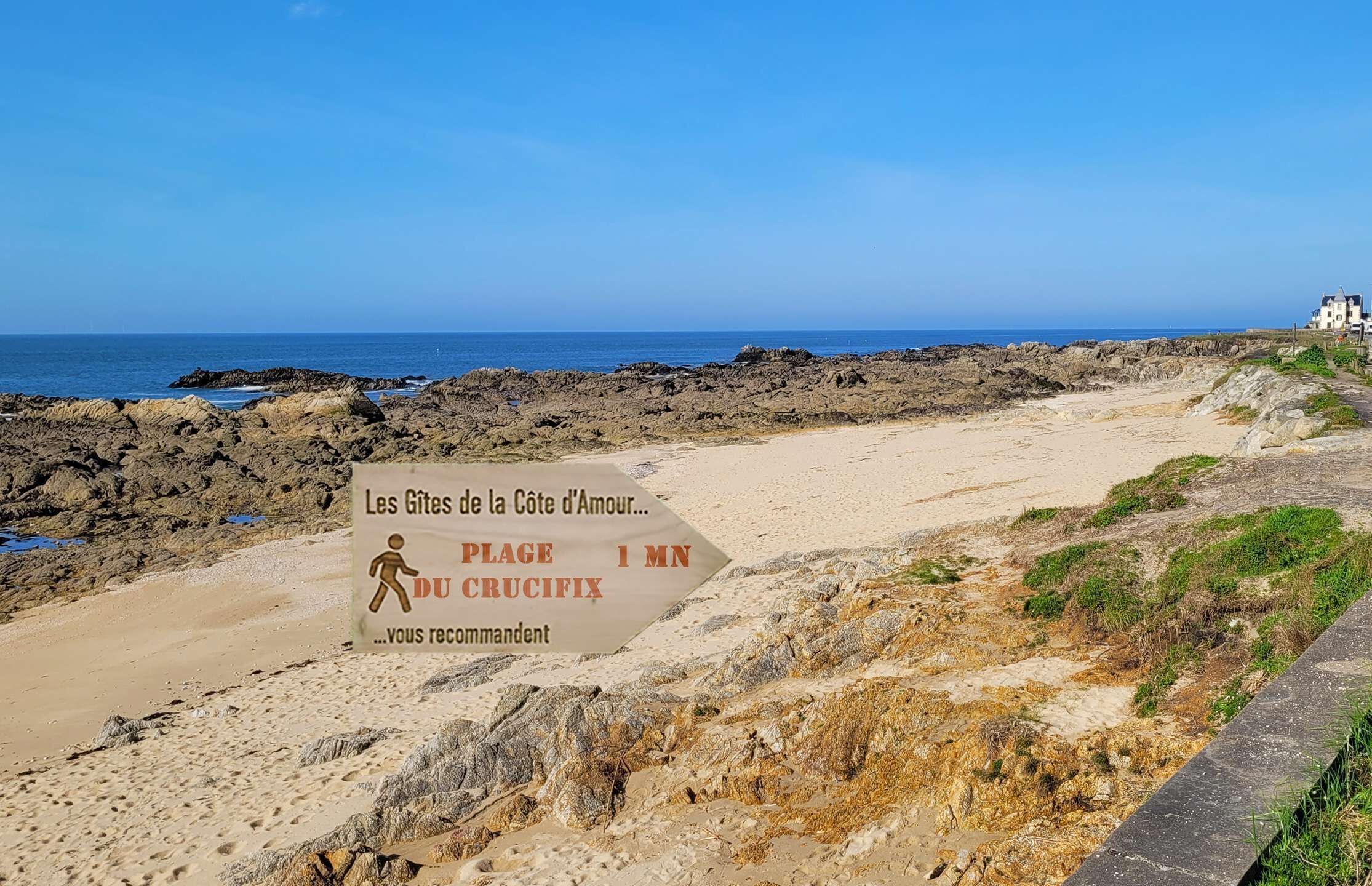 Une plage avec un panneau indiquant qu’il faut marcher 1 km pour rejoindre les gîtes de la Côte d’Amour.