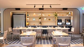 A modern dining area with long tables, white chairs, and a patterned floor.