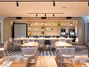 A modern dining area with multiple tables and chairs, a kitchen area with appliances, and decorative shelves. - Ibis Darwin Airport Hotel (Eaton)