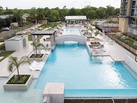 A large swimming pool with a bridge, surrounded by lounge areas and palm trees.