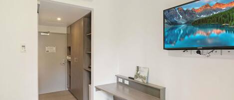 A modern hotel room with a large flat-screen TV mounted on the wall, a wooden desk, and a cozy seating area.