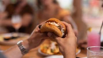 A person holding a sandwich with a bun, with a blurred background of other people.