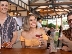 A group of people seated at a bar with a wooden table, a high ceiling, and a view of the outdoors. - Ibis Darwin Airport Hotel (Eaton)