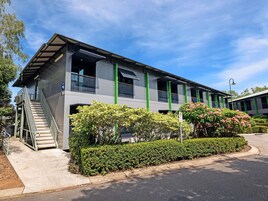 A modern building with a staircase leading to an entrance, surrounded by well-maintained hedges and a clear sky.
