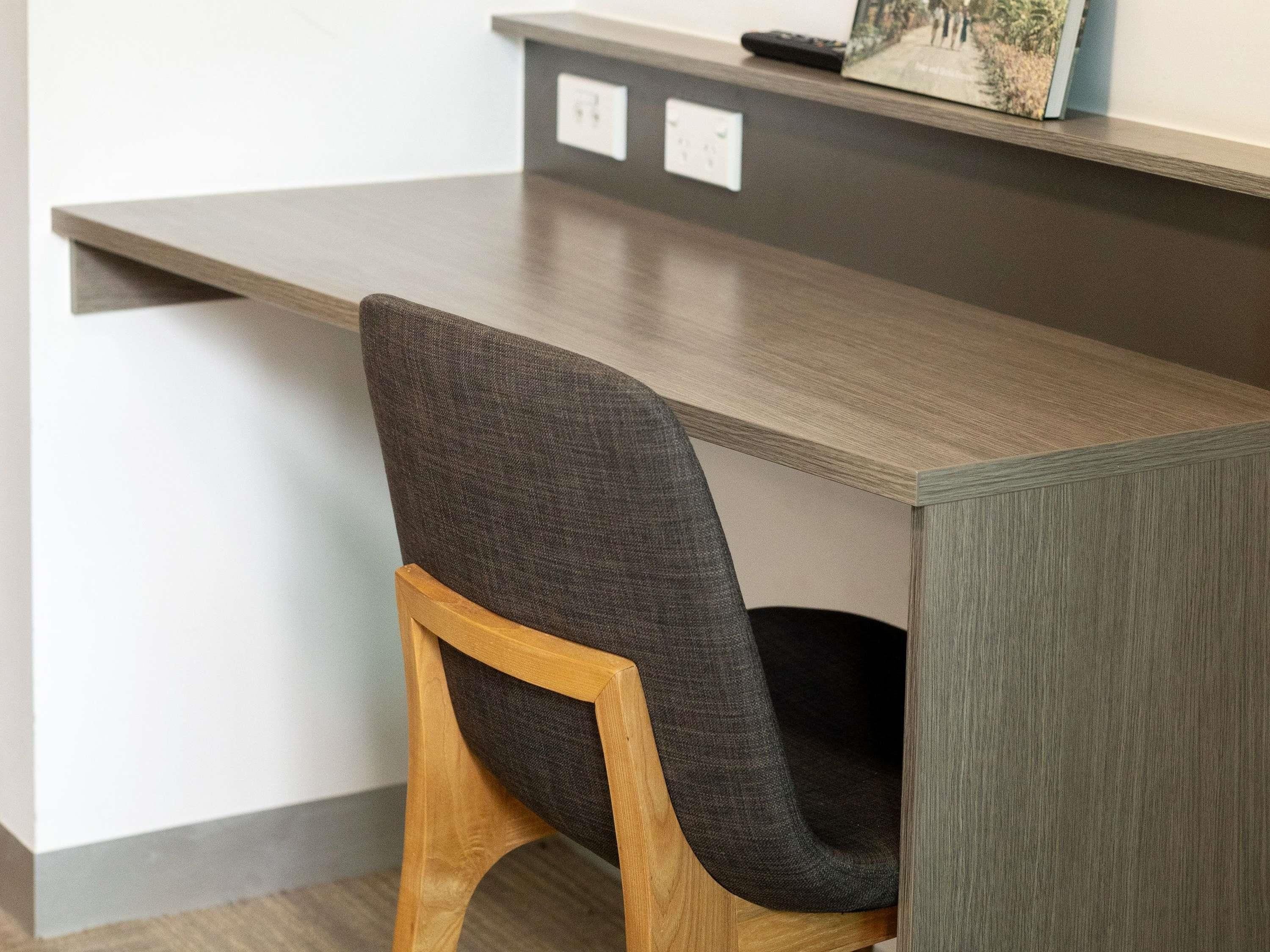 A modern desk with a wooden frame and a dark grey upholstered chair.