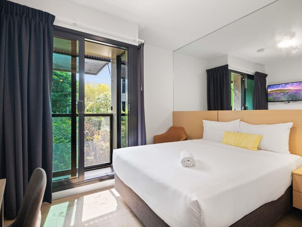 A hotel room with a large bed, a flat-screen TV, a window with curtains, and a view of greenery outside. - Ibis Darwin Airport Hotel (Eaton)