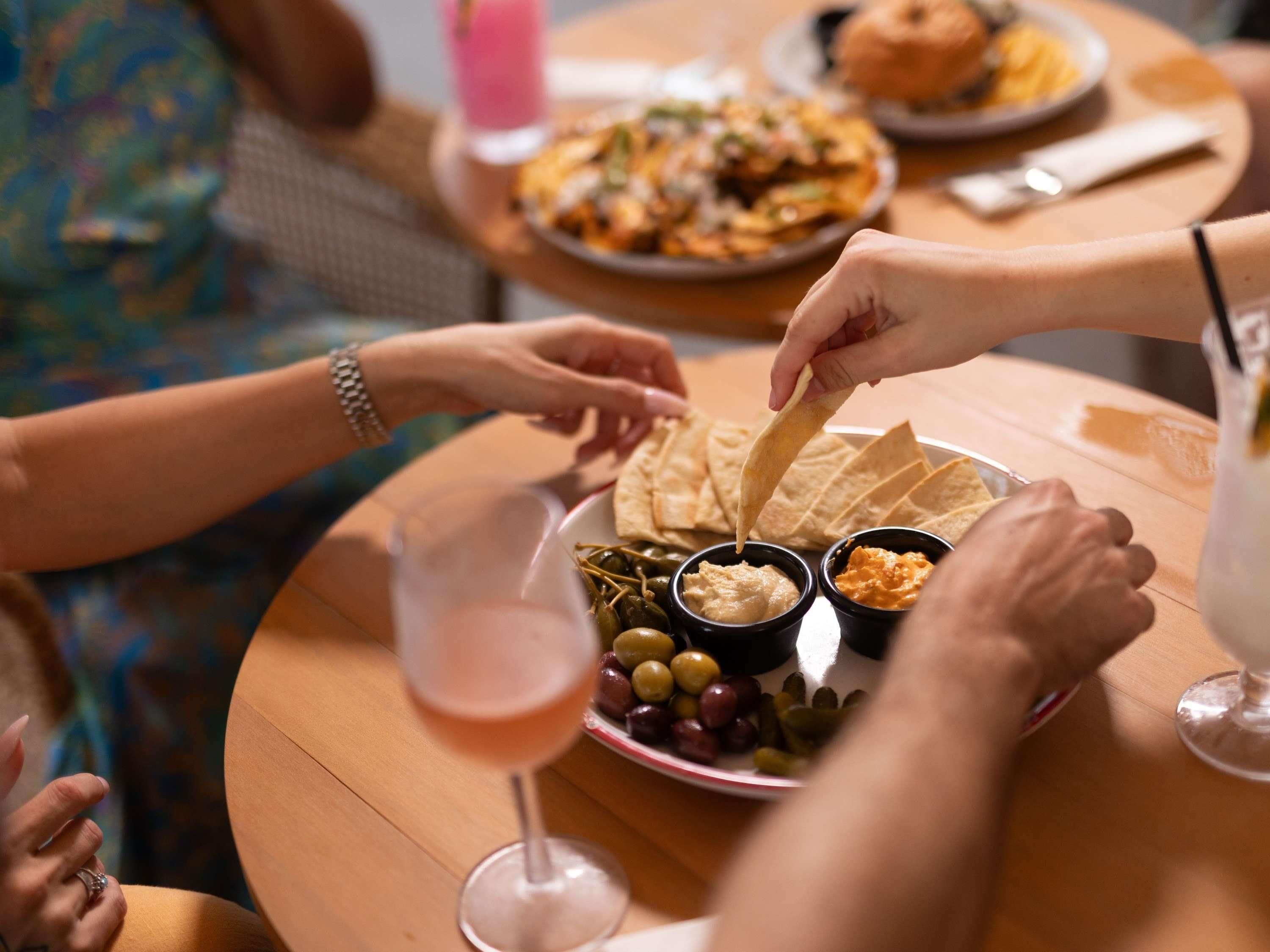 Un grupo de personas cenando en una mesa redonda, con un plato de aperitivos, incluyendo papas fritas y salsas, y un vaso de bebida.