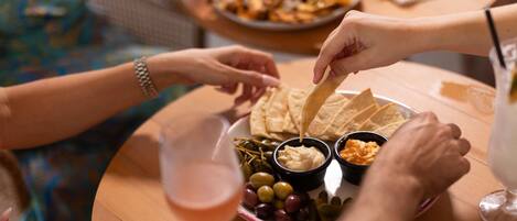 Un grupo de personas cenando en una mesa redonda, con un plato de aperitivos, incluyendo papas fritas y salsas, y un vaso de bebida.