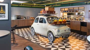 Un coche antiguo estacionado en una cocina moderna con suelo de diseño geométrico, armarios de madera y una encimera con productos alimenticios.