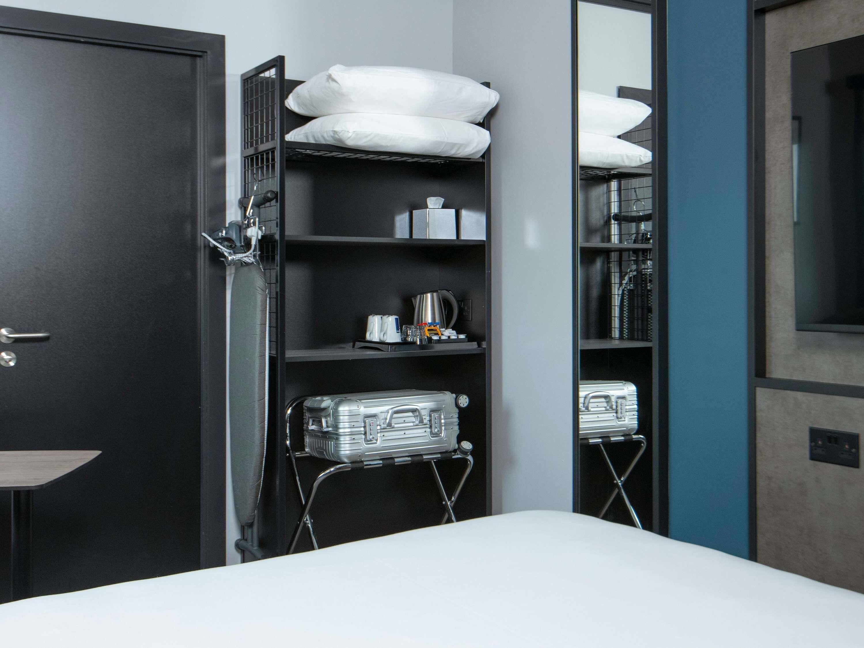 Habitación de hotel con cama, armario y estante con artículos de aseo.