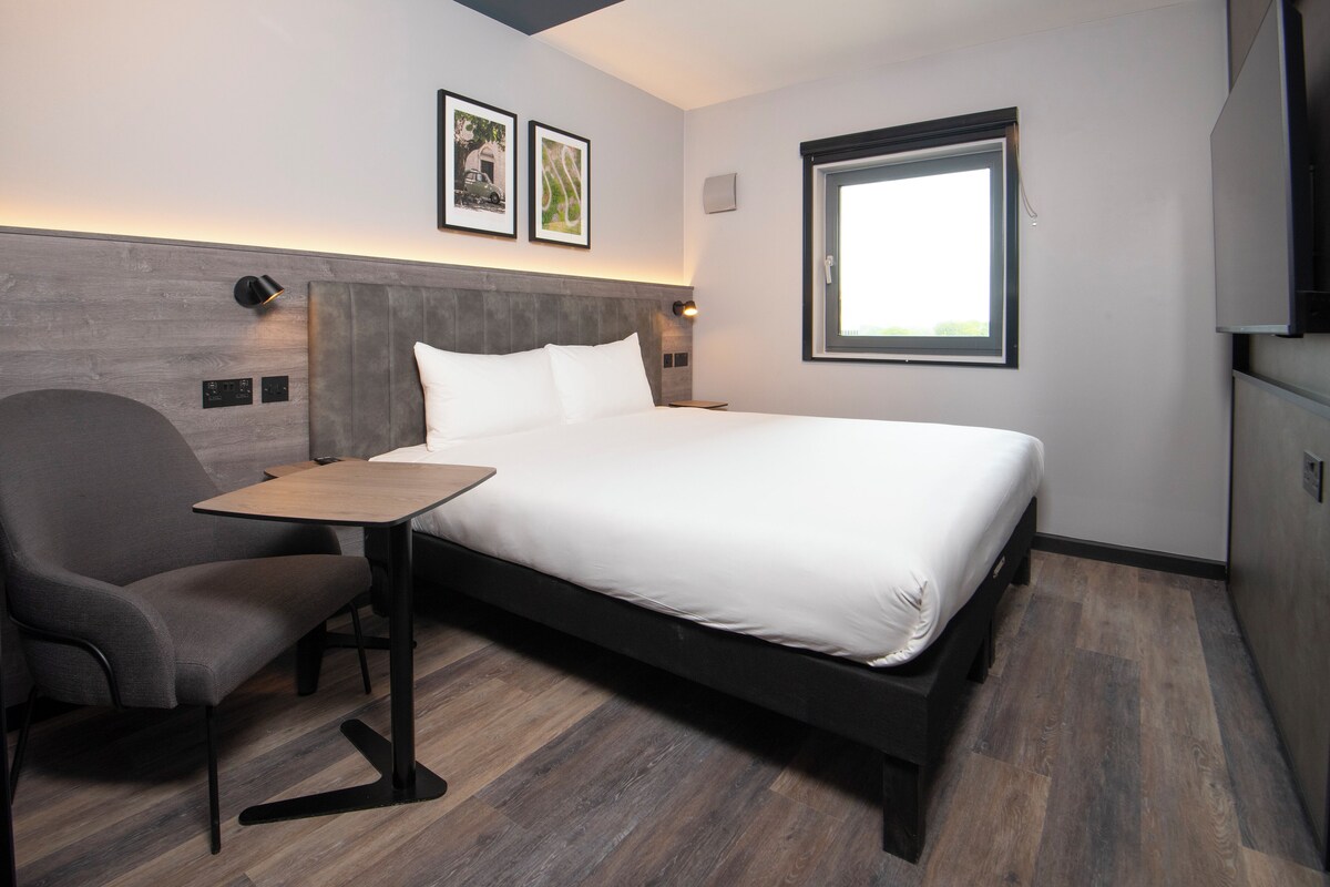 Una habitación de hotel moderna con una cama, un escritorio, una silla y un ventanal.